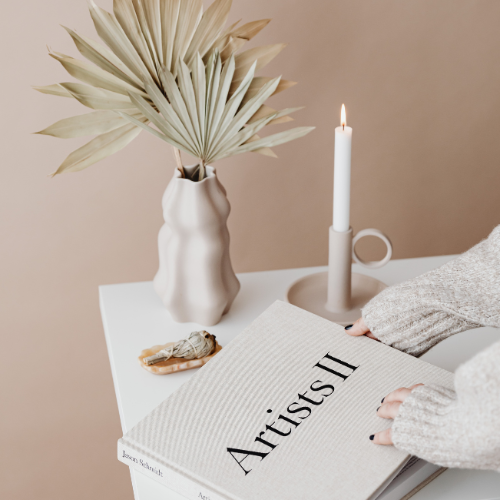 A dispaly of home decor with a vase, candle and coffee table book on a table